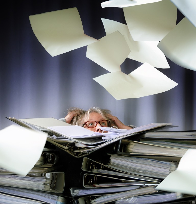 Desperate woman sinks behind stacks of ring binders on an office desk