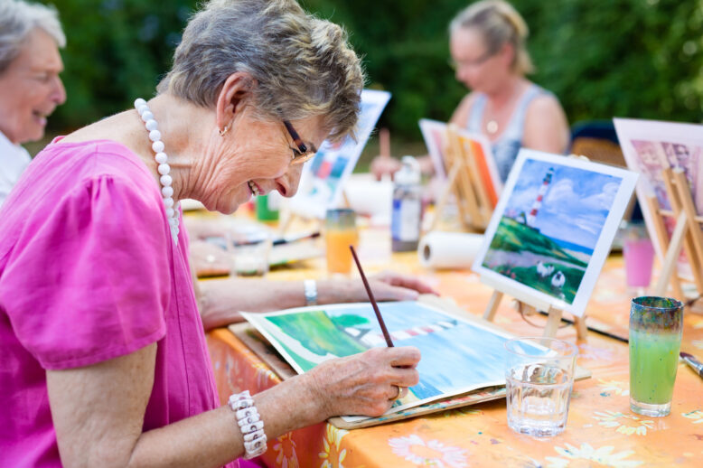 Senior women painting outside at a table.