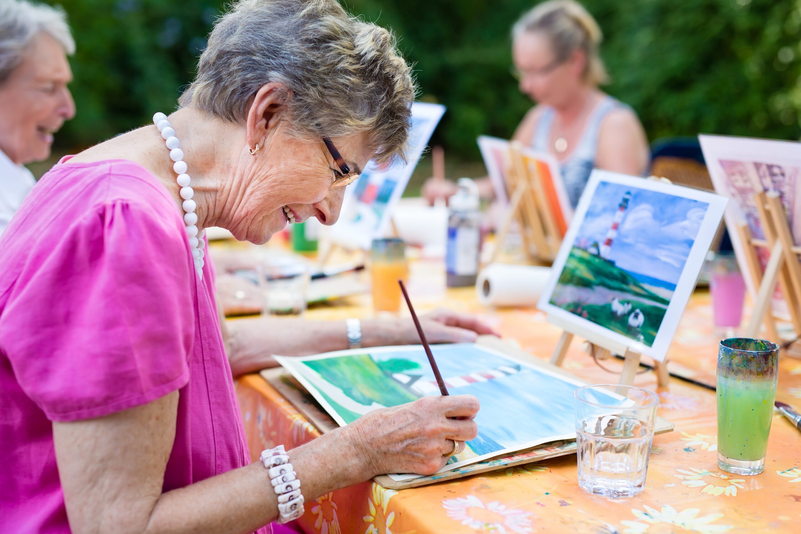 Senior women painting outside at a table.