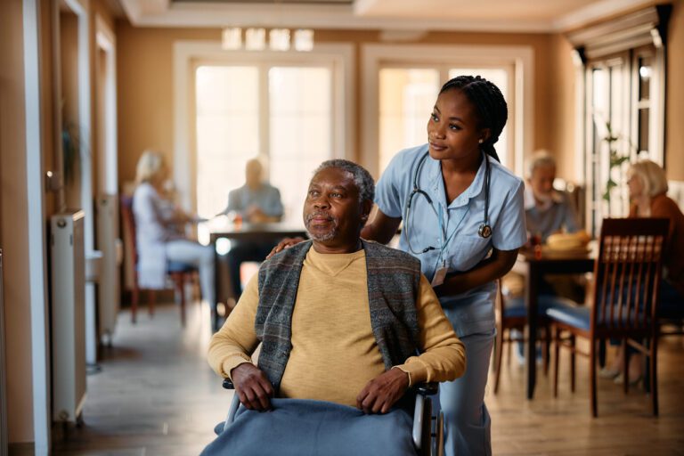 The Vital Role of Caregivers African American senior in wheelchair and young nurse looking through the window at residential care home.