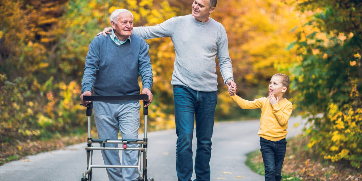 Elderly father adult son and grandson out for a walk in the park. Unpaid Caregivers Should Be Paid!